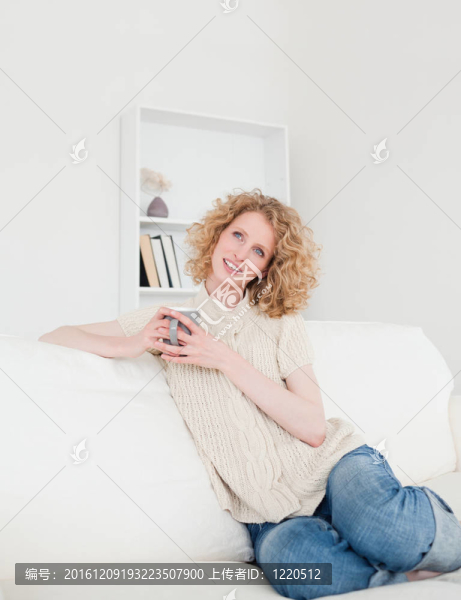 漂亮的金發(fā)女郎坐在她公寓的沙發(fā)上享受著一杯咖啡