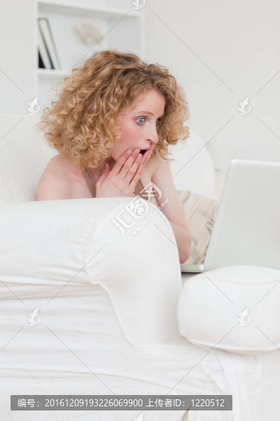 開朗的金發(fā)女人放松她的筆記本電腦坐在她公寓的沙發(fā)上
