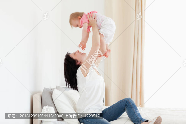 迷人的黑發(fā)女人玩她的寶寶坐在她房間里的床上
