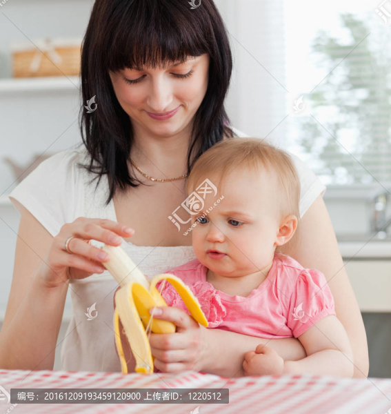 迷人的黑發(fā)女人剝香蕉，抱著她的孩子跪在廚房