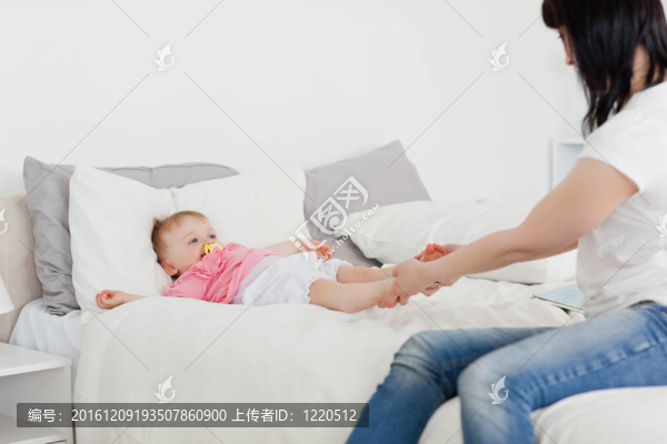 可愛的黑發(fā)女人玩她的寶寶坐在她房間里的床上