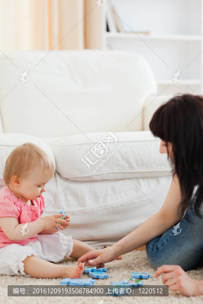 迷人的女人和她的寶寶玩拼圖碎片，而坐在客廳的地毯上