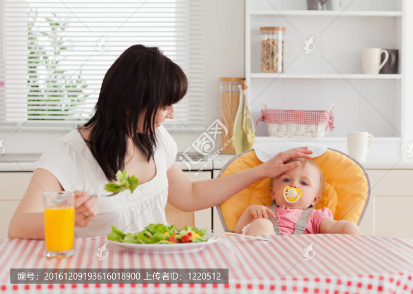 美麗的黑發(fā)女人吃沙拉在她旁邊的寶寶坐在廚房
