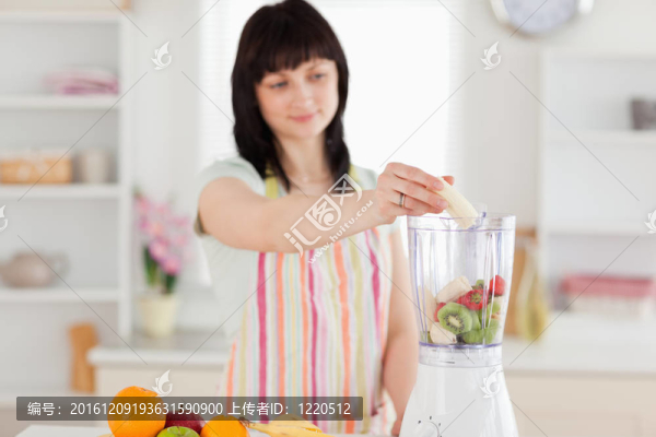 漂亮的黑發(fā)女人把蔬菜放在一個(gè)攪拌機(jī)