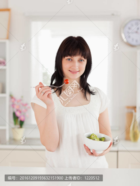 可愛的黑發(fā)女性吃櫻桃番茄在廚房里端著一碗蔬菜