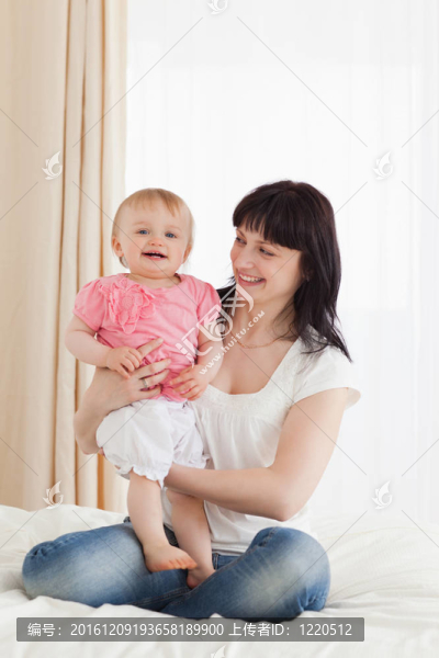 可愛的黑發(fā)女人抱著她的孩子在她的膝蓋上坐在她的公寓床