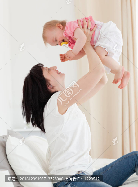 漂亮的黑發(fā)女人玩她的寶寶坐在她的公寓床