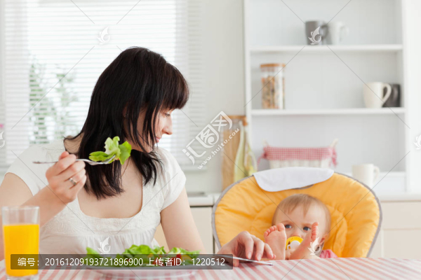 美麗的黑發(fā)女人吃沙拉在她旁邊的寶寶坐在廚房