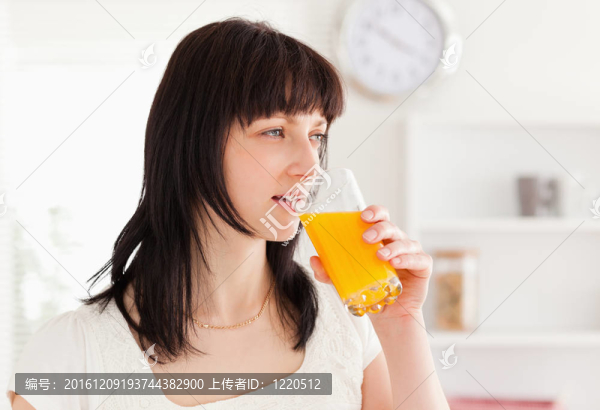 好看的女人站在廚房的同時喝一杯橙汁