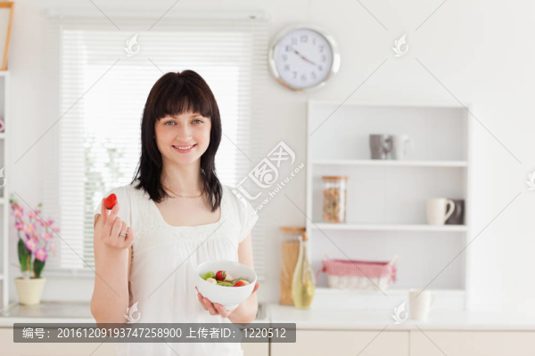迷人的黑發(fā)女性吃櫻桃番茄在廚房里端著一碗蔬菜