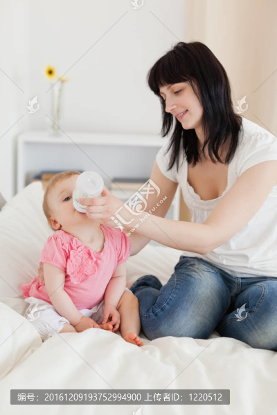 漂亮的黑發(fā)女瓶喂她的嬰兒床上