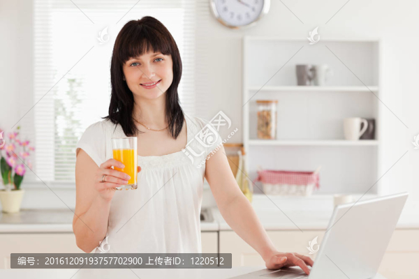 華麗的黑色的女人拿著一杯橙汁而輕松的在廚房里用她的筆記本電腦