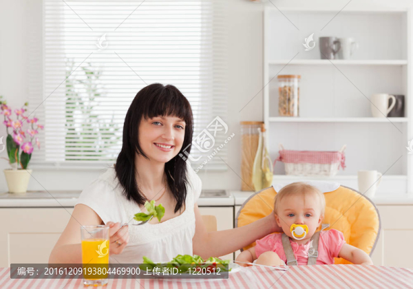 迷人的黑發(fā)女人吃沙拉在她旁邊的寶寶坐在廚房