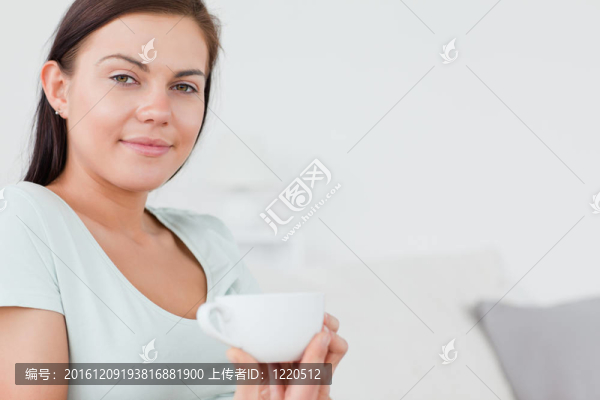一個(gè)迷人的女人坐在沙發(fā)上喝著一杯茶看著相機(jī)