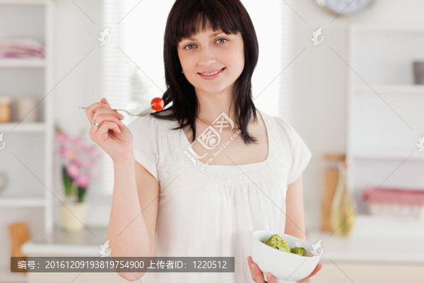 漂亮的黑發(fā)女性吃櫻桃番茄在廚房里端著一碗蔬菜