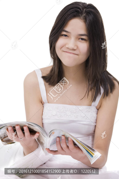 漂亮的年輕少女穿著白色的連衣裙坐著看雜志，表情滑稽；