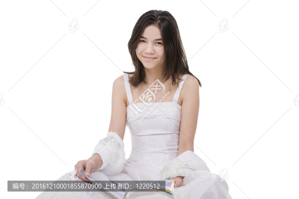 美麗的年輕少女穿著白色的連衣裙坐在雜志上看書；在白色上孤立
