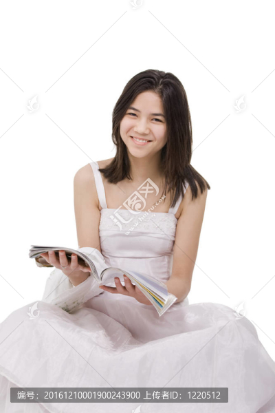 美麗的年輕少女穿著白色的連衣裙坐在雜志上看書；在白色上孤立