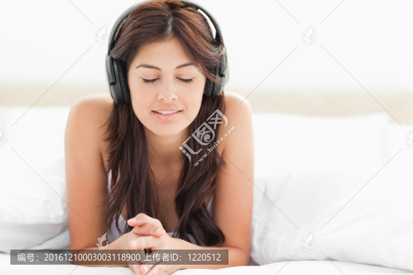 一個女人在床上閉著眼睛專心地聽著耳機上的音樂。