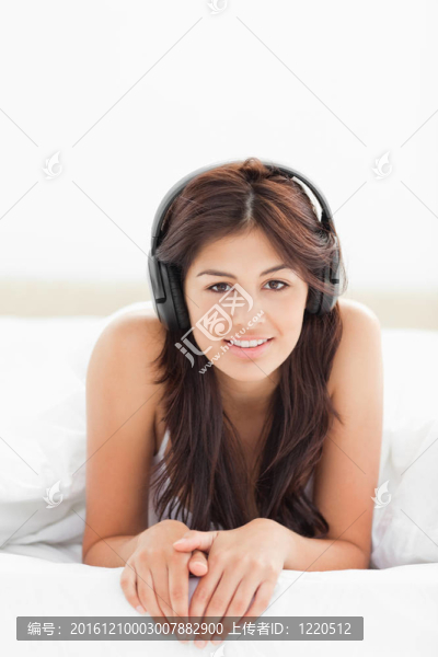 一個女人躺在床下的被子里聽著音樂，雙手合十，臉上掛著微笑。