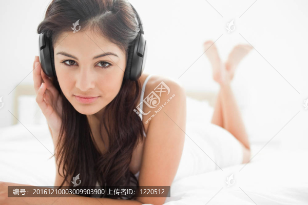 一個女人在床上，雙腿交叉；聽耳機，一只手壓在他們的身邊。