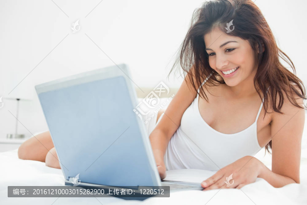 一個(gè)女人躺在她的床上，微笑著享受著筆記本上的東西。