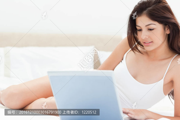 一個(gè)女人用她的筆記本電腦在她面前瀏覽，而她躺在她的床上。