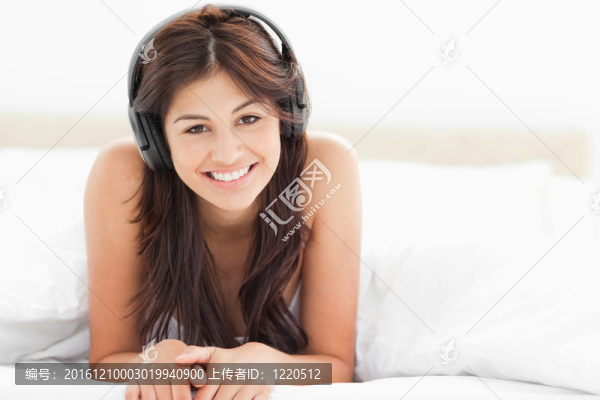 一個(gè)面帶微笑的女人，頭歪了，在床的盡頭聽著音樂。