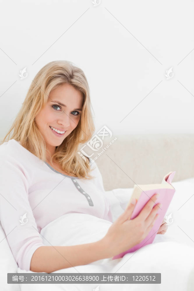一個(gè)女人筆直地坐在床上；拿著她的書，向旁邊看了一眼。