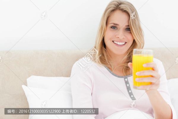 一個(gè)女人拿著一杯桔子汁微笑著向前看；而在床上。