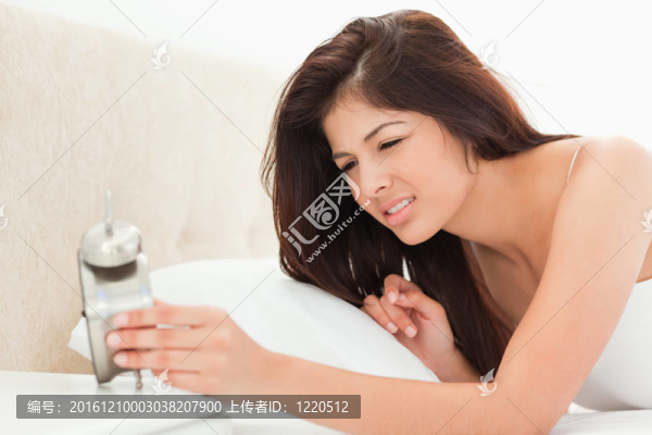 一個(gè)女人的覺醒和檢查自己的時(shí)鐘。她累了，因?yàn)樗难劬雌饋砗苤亍? title=