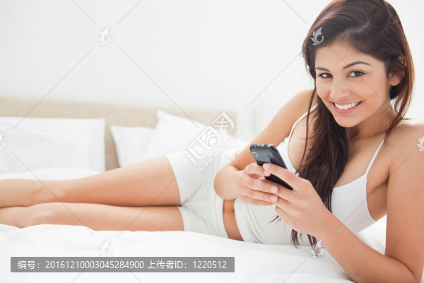 女人躺在床上微笑，因?yàn)樗弥悄苁謾C(jī)