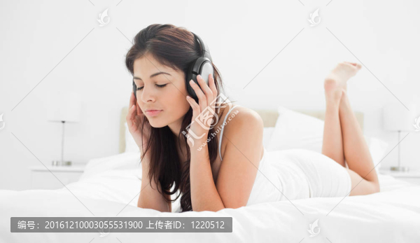 一個(gè)女人在臥室里閉著眼睛，聽(tīng)著耳機(jī)上的音樂(lè)，雙手放在耳機(jī)上。