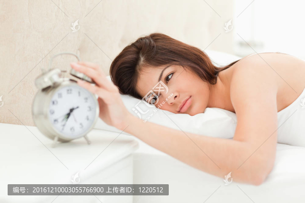 一個女人躺在床上，手放在附近鬧鐘的鐘上，停止了它的鈴聲。