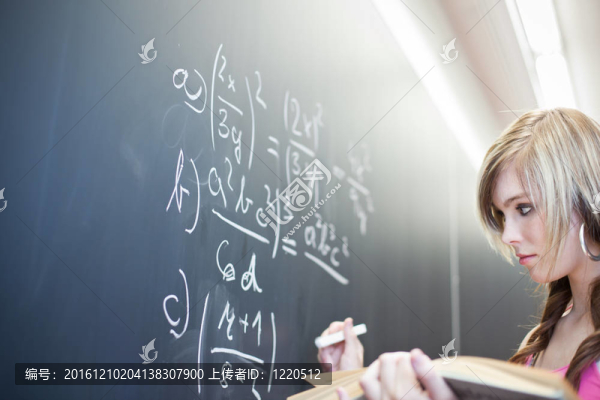 年輕漂亮的大學生寫在黑板上/黑板上數(shù)學課期間（淺景深；顏色色調(diào)的圖像）