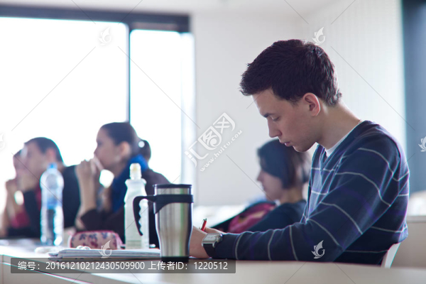 年輕的；英俊的男大學生坐在教室里擠滿了學生在課堂上（顏色色調(diào)的圖像；淺景深）
