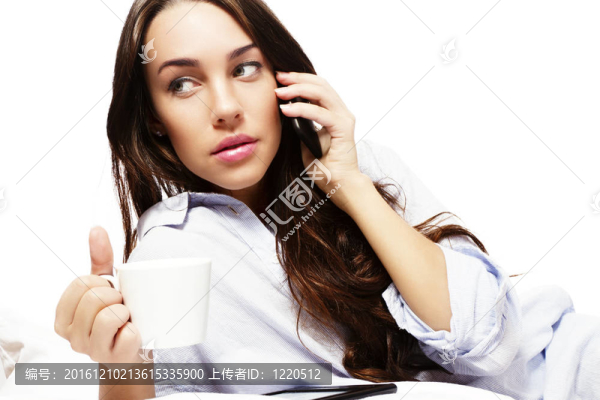 美麗的女人在床上拿著咖啡，一邊用白色背景電話(huà)