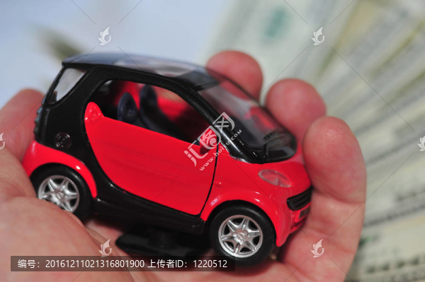 一只手拿著黑色和紅色的汽車在白色的許多鈔票上（選擇性聚焦）。