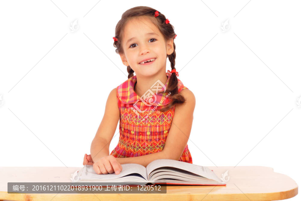 微笑的小女孩在書桌上看書；在白色上孤立