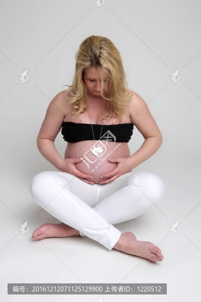 一個懷孕的年輕婦女坐在那里，抱著她的肚子看著它。女人是戴著一頂黑色的和白色的奇諾光著腳