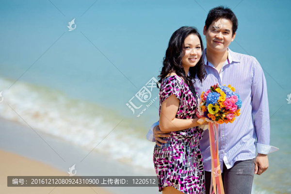 迷人的情侶站在沙灘上，帶著美麗的花束