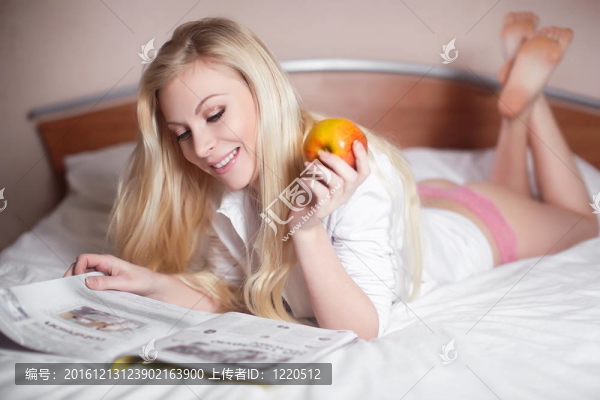 美麗性感性感微笑年輕金發(fā)女郎躺在床上看雜志與蘋果