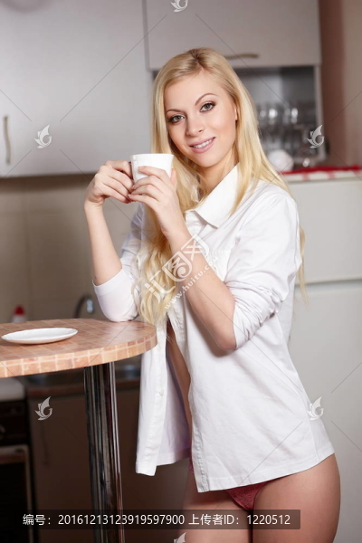 年輕漂亮的女人拿一杯咖啡在廚房