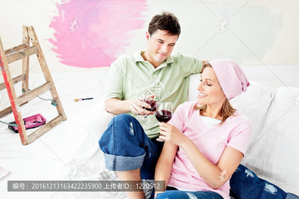 高興的白人夫婦躺在沙發(fā)上喝葡萄酒后，在他們的新房子畫一個房間
