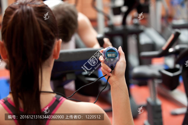年輕的女人抱著一個(gè)計(jì)時(shí)器和人在健身中心鍛煉身體
