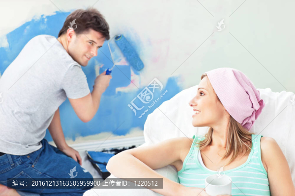 漂亮的女人在沙發(fā)上放松，而男朋友在他們的新房子粉刷房間