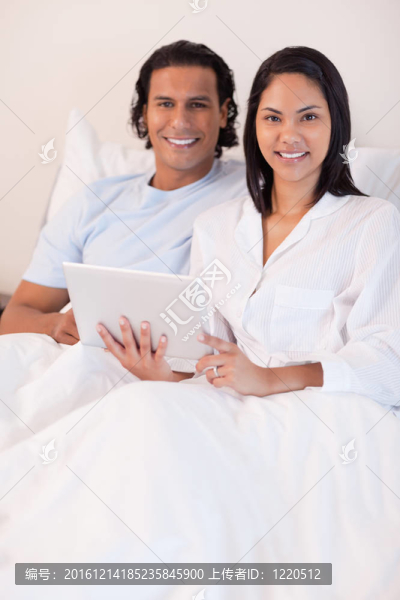 夫婦在他們的床上使用平板電腦