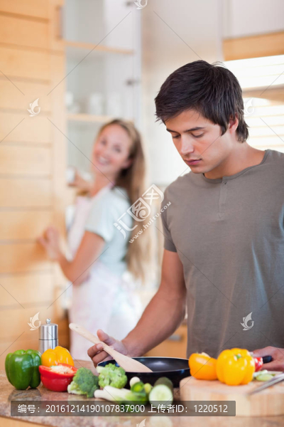 一個男人做飯的肖像，而他的妻子正在洗碗