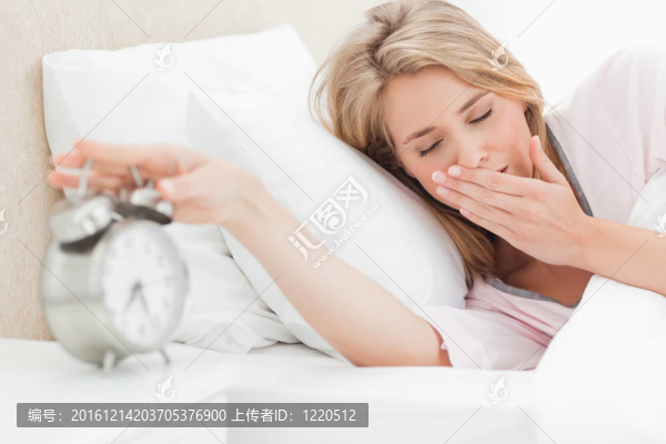 一個(gè)女人在床上移動(dòng)她的手關(guān)閉她的報(bào)警，而她的眼睛是封閉的