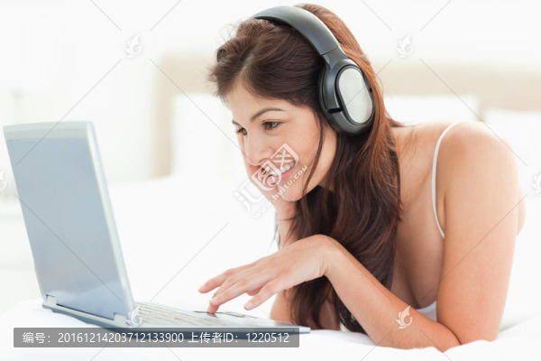 一個女人一邊戴著耳機一邊微笑著，在筆記本上敲打鼠標墊，一邊在床上放松。